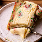 A bite missing from a slice of sugar cookie cheesecake on a plate.