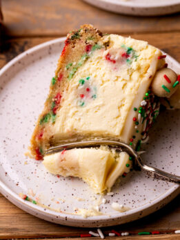 A bite missing from a slice of sugar cookie cheesecake on a plate.