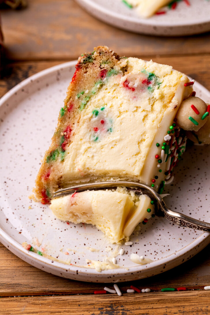 A bite missing from a slice of sugar cookie cheesecake on a plate.