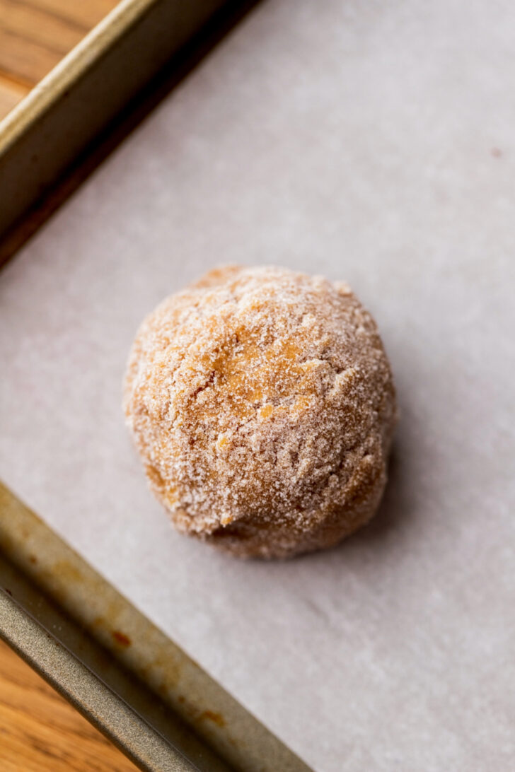 Cookie dough ball rolled in sugar on a cookie sheet.