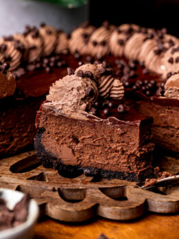 A slice of triple chocolate cheesecake on the wood platter.