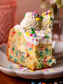 Slice of funfetti cake cheesecake with a bite missing.