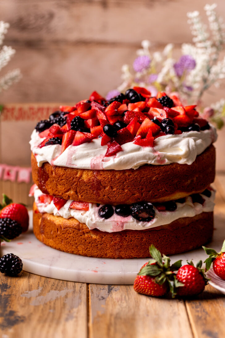Decorated berries and cream cake on a platter.