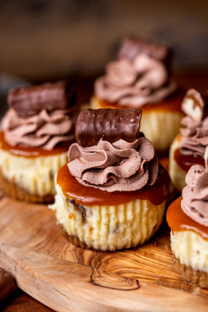 Decorated Twix mini cheesecakes on a wood board.